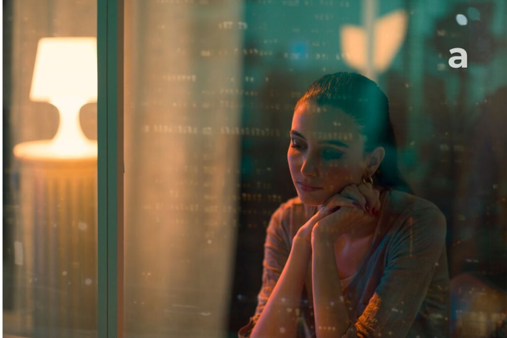 Woman sitting by a window reflecting on the life she keeps waiting to start